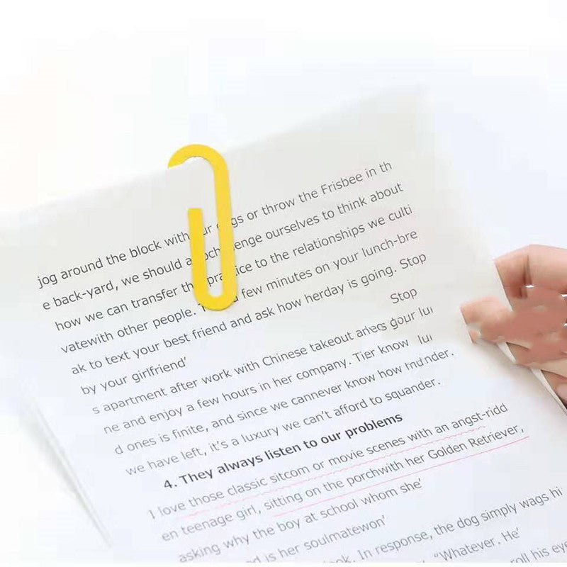 Yellow U-shaped paper clip bookmark securing an open page with a hand