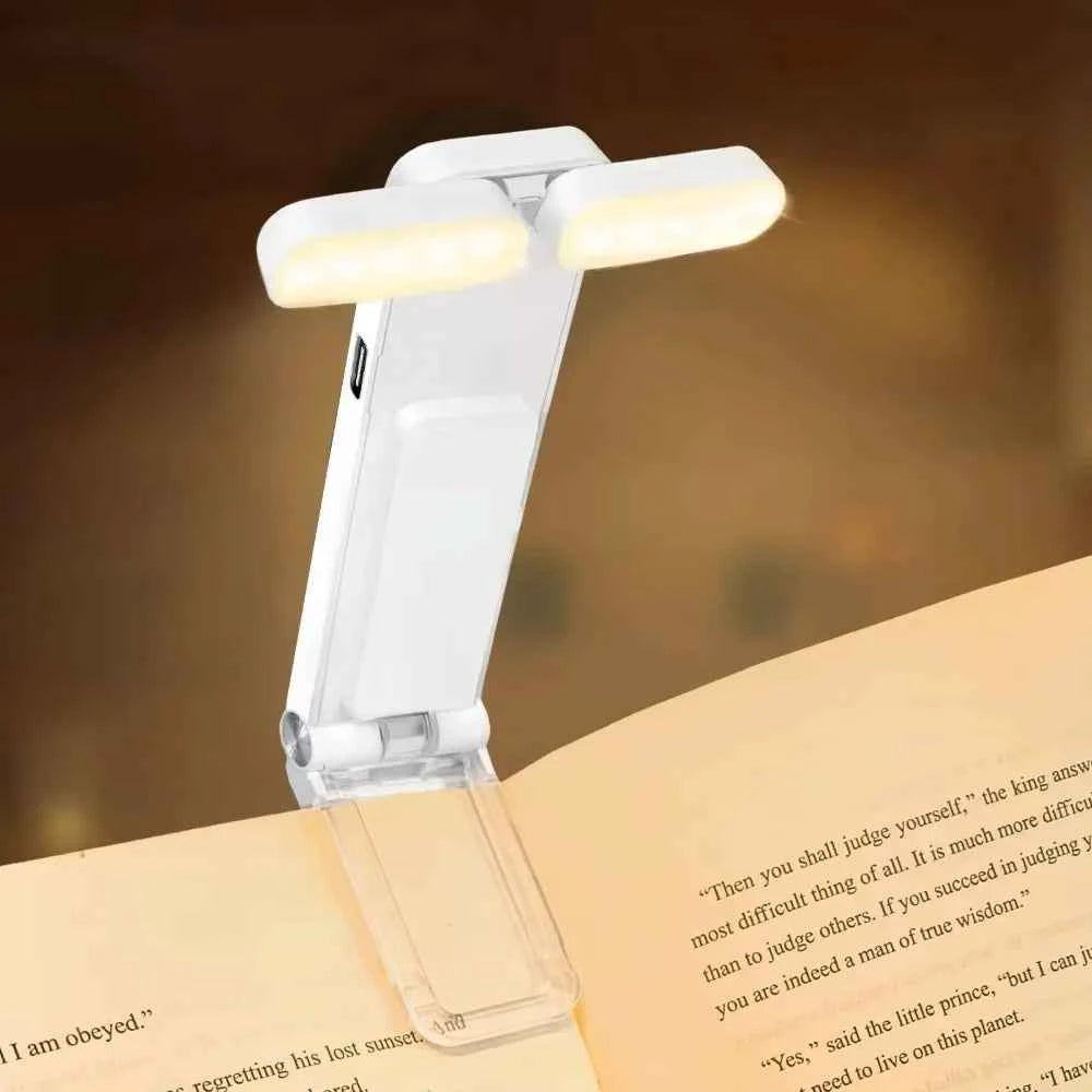 White clip-on book light angled over pages, twin LED bars glowing above clear clamp