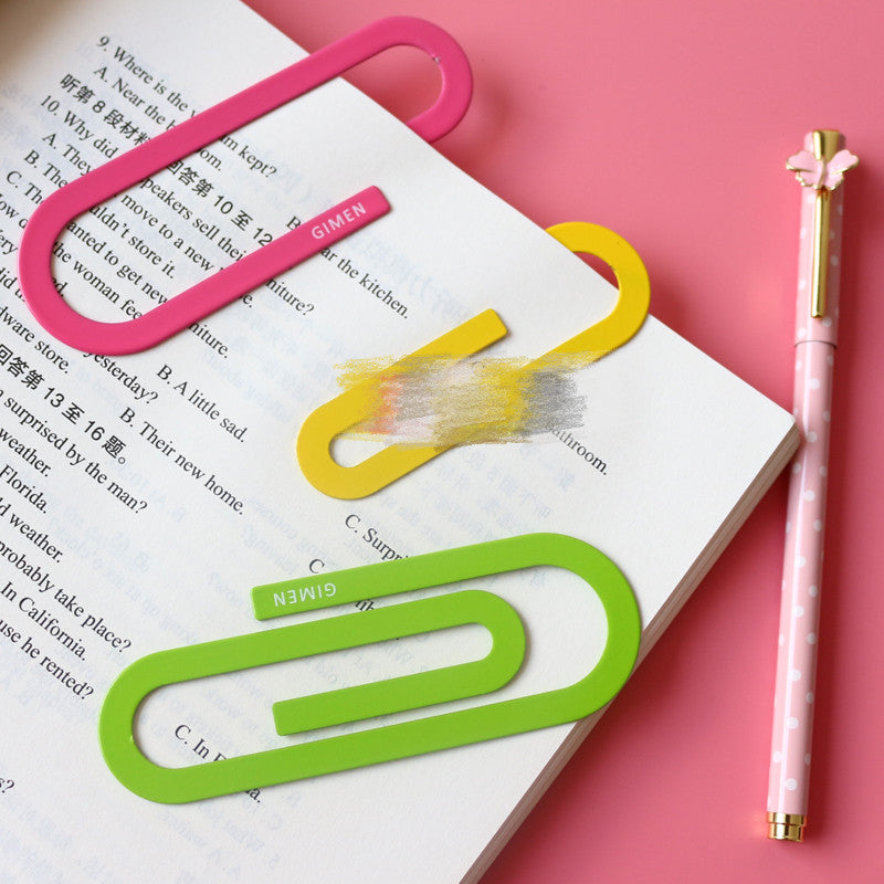 Big paper clip bookmarks in pink, yellow, and green on an open book