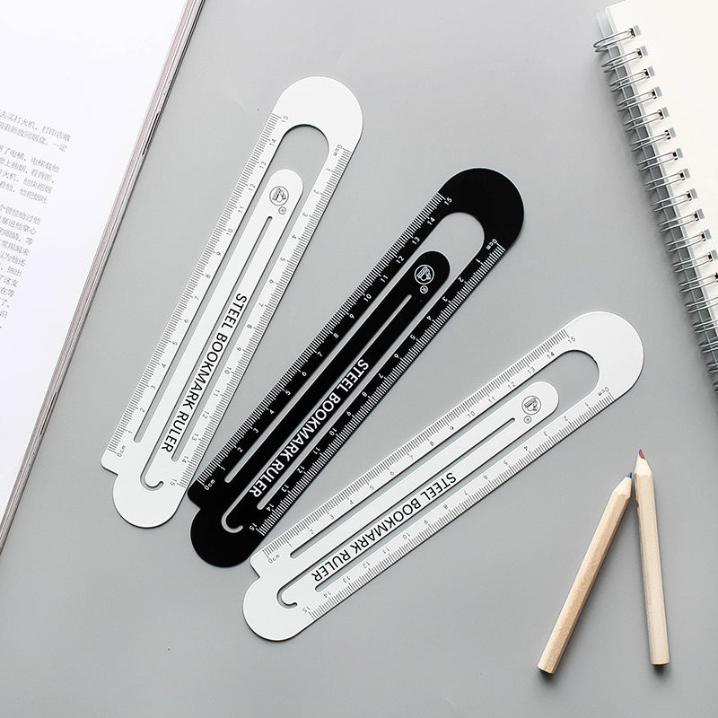 Hollow steel bookmark rulers, black and white 12 cm, with pencils on study pages.